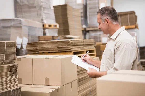 hombre realizando un control de inventarios en su almacén lleno de cajas