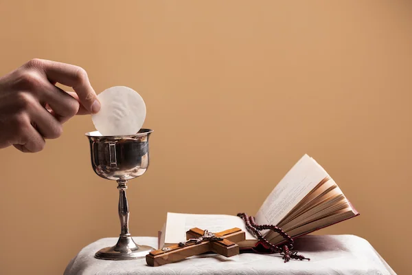 primer plano de mano remojando hostia en el vino y con una biblia abierta