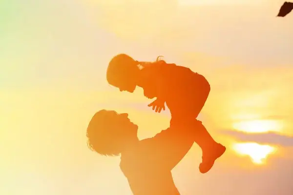 padre cargando a su hijo frente a un atardecer