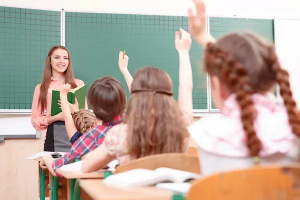 alumnos levantando la mano para participar en clase mientras profesora los mira con alegría